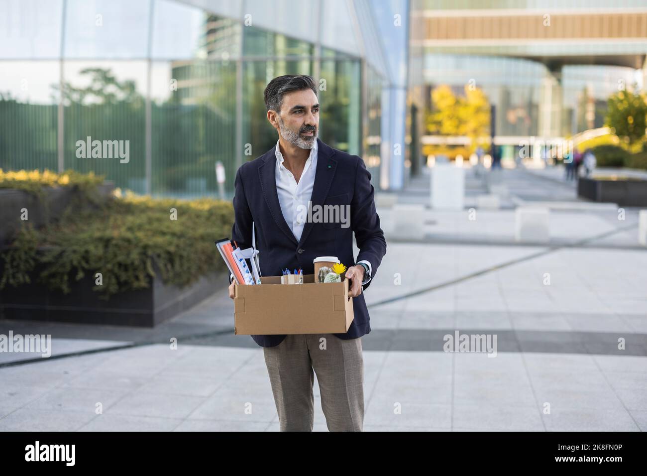 Businessman with office supply in box standing on footpath Stock Photo