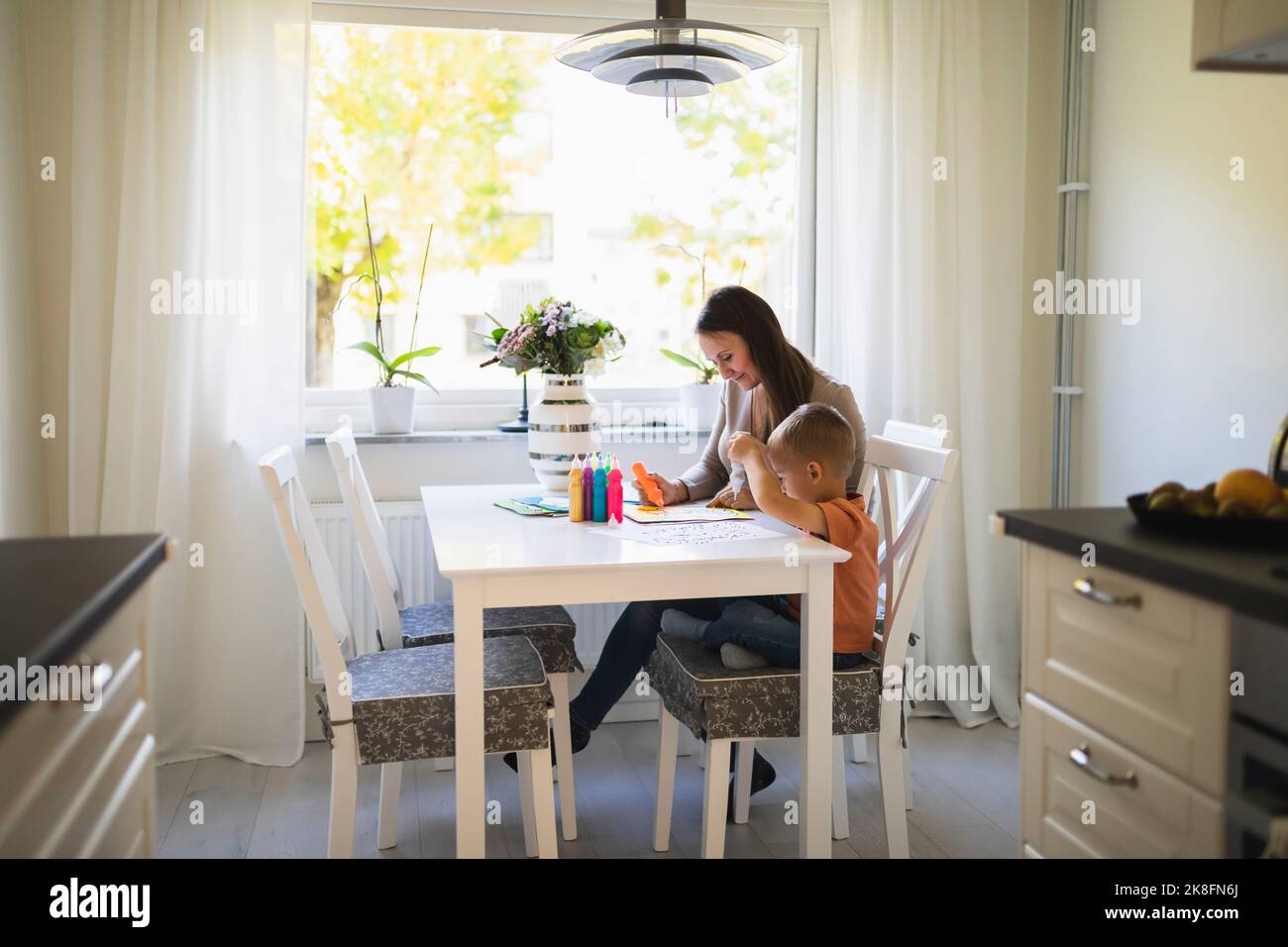 Mother and son using paint tubes in coloring book on dining table at home Stock Photo