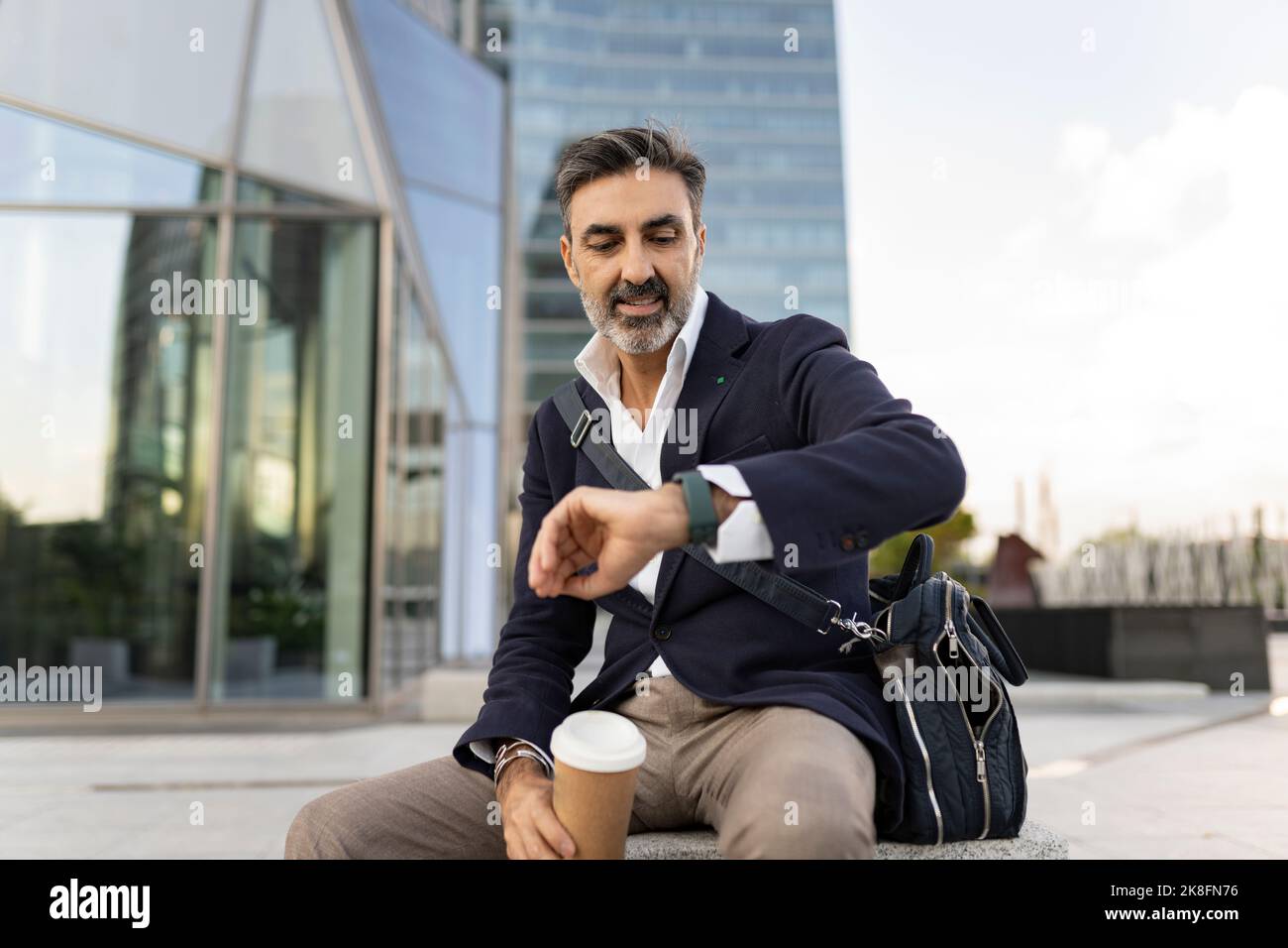 Mature businessman checking time on wristwatch sitting in front of ...