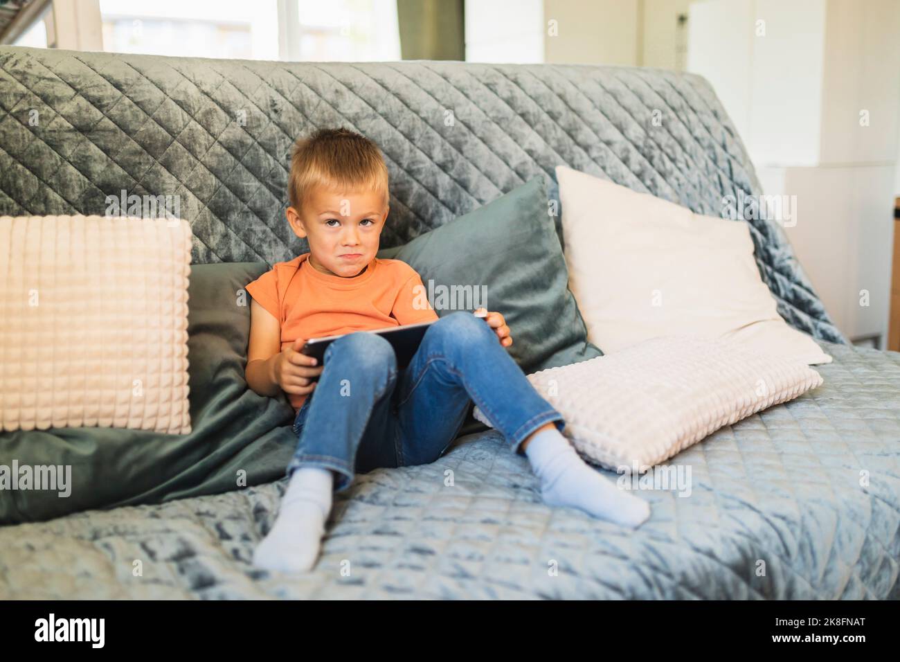 Cute boy with tablet PC sitting on sofa at home Stock Photo