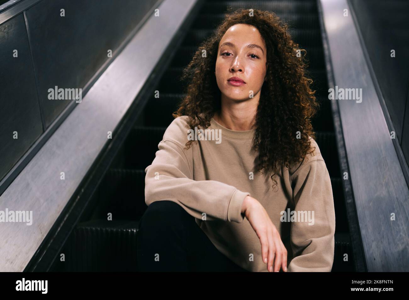 Young woman sitting on escalator Stock Photo