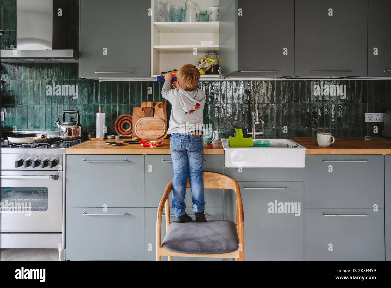 Boy searching in kitchen cabinet standing on chair at home Stock Photo