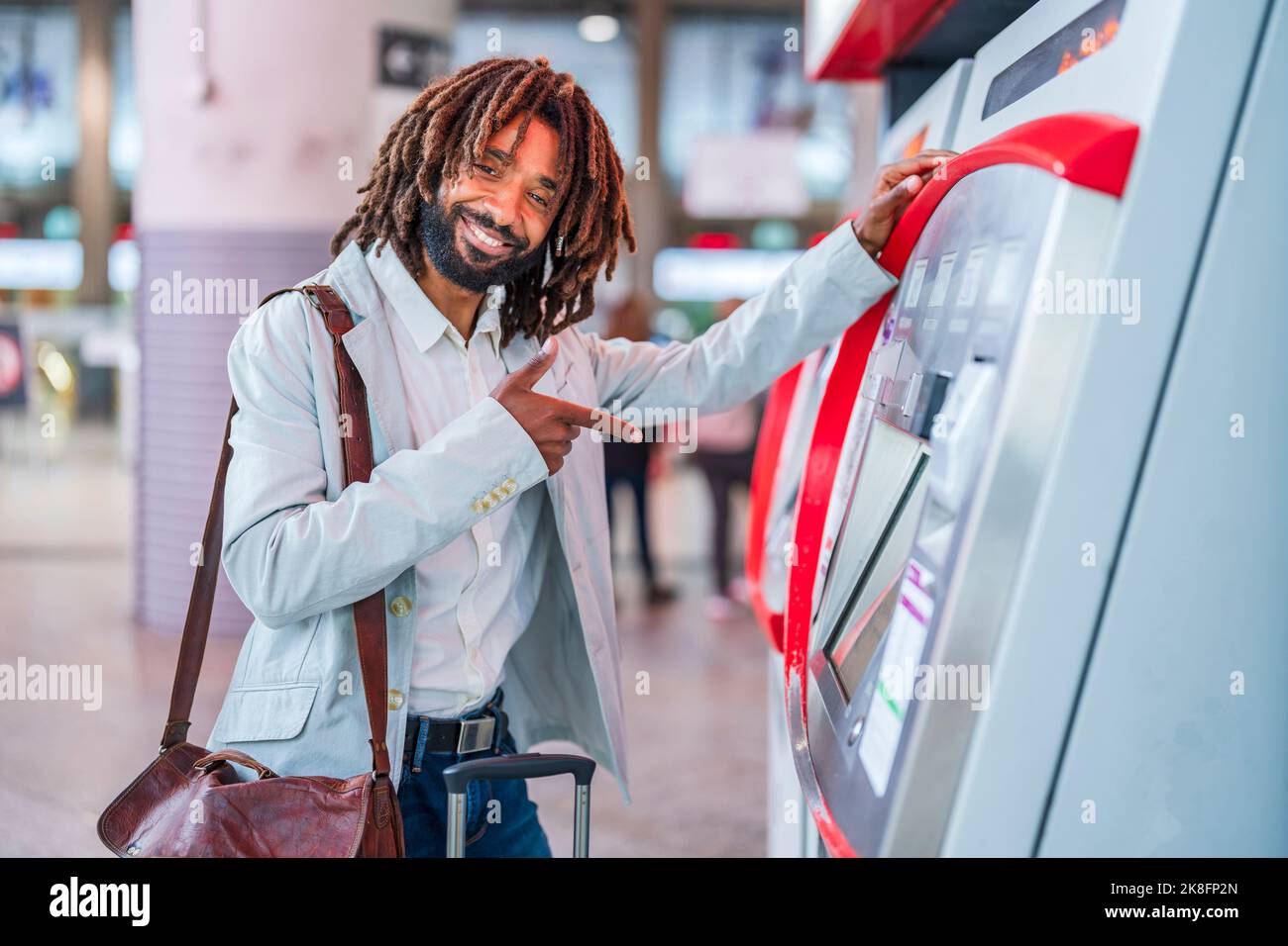 Happy businessman with luggage pointing at ticket machine in station Stock Photo