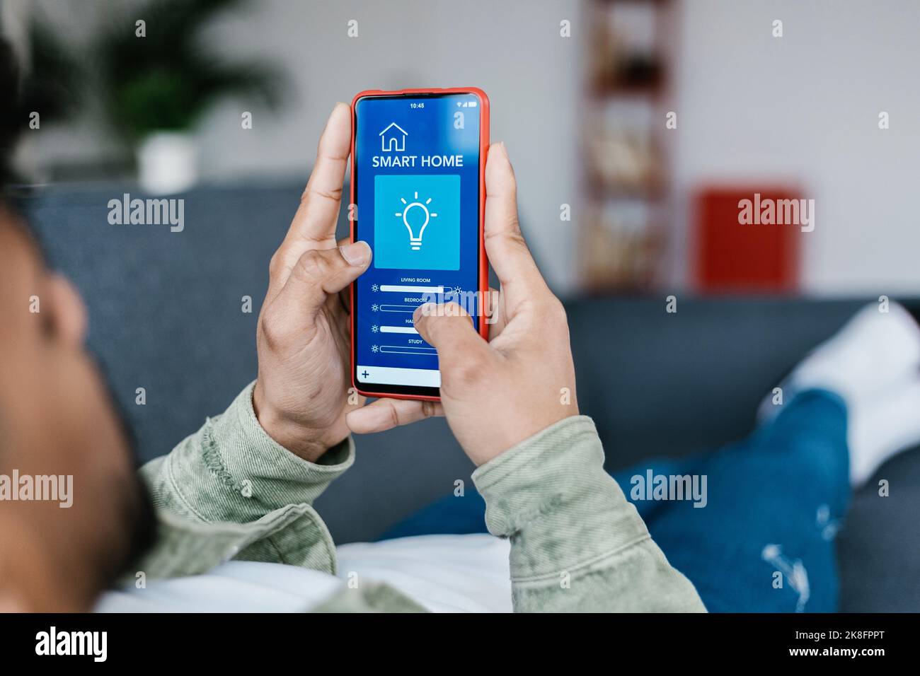 Young adult man using IOT automation app on smart phone dimming the