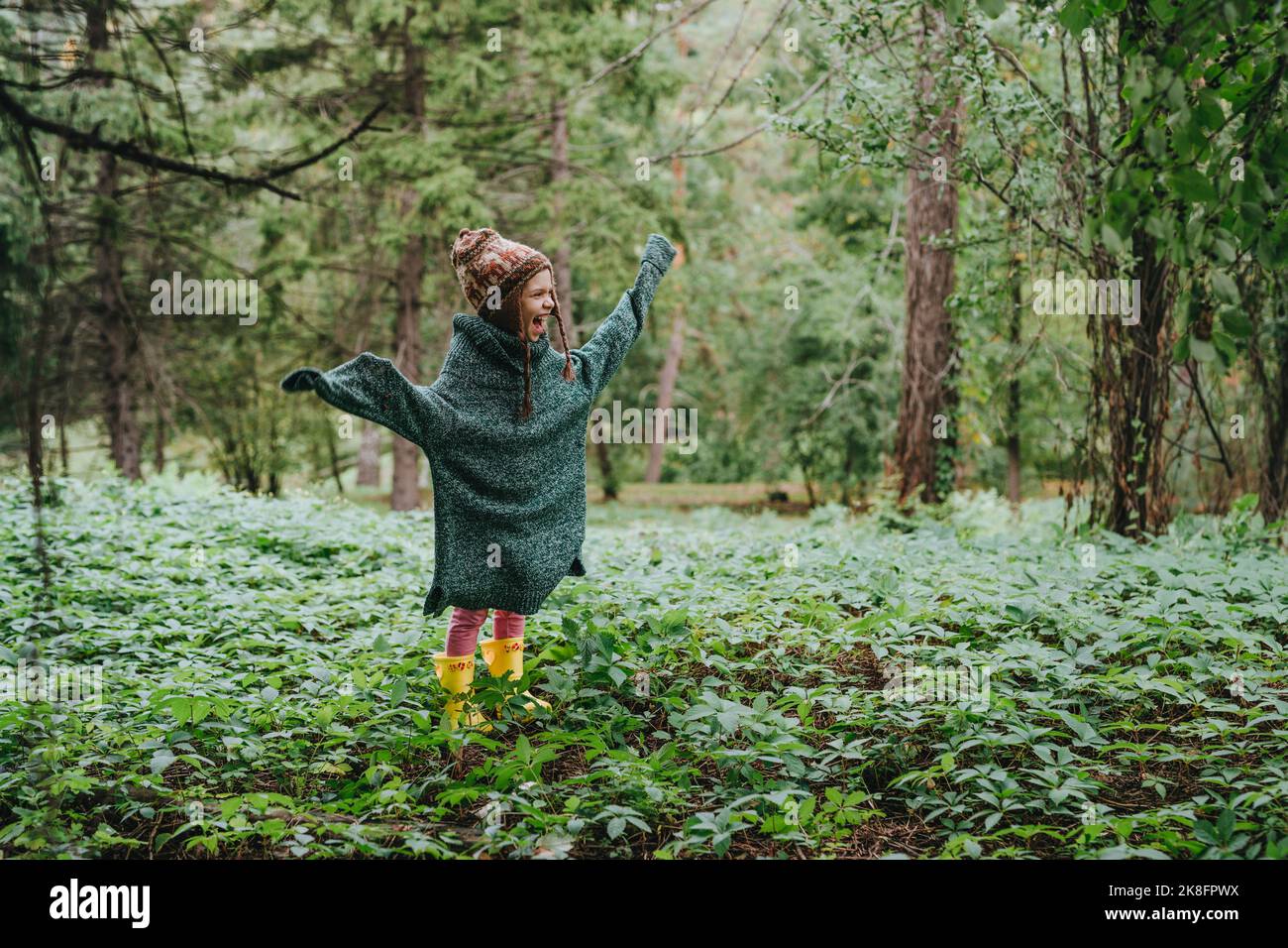 Happy girl in oversized sweater standing amidst forest Stock Photo - Alamy