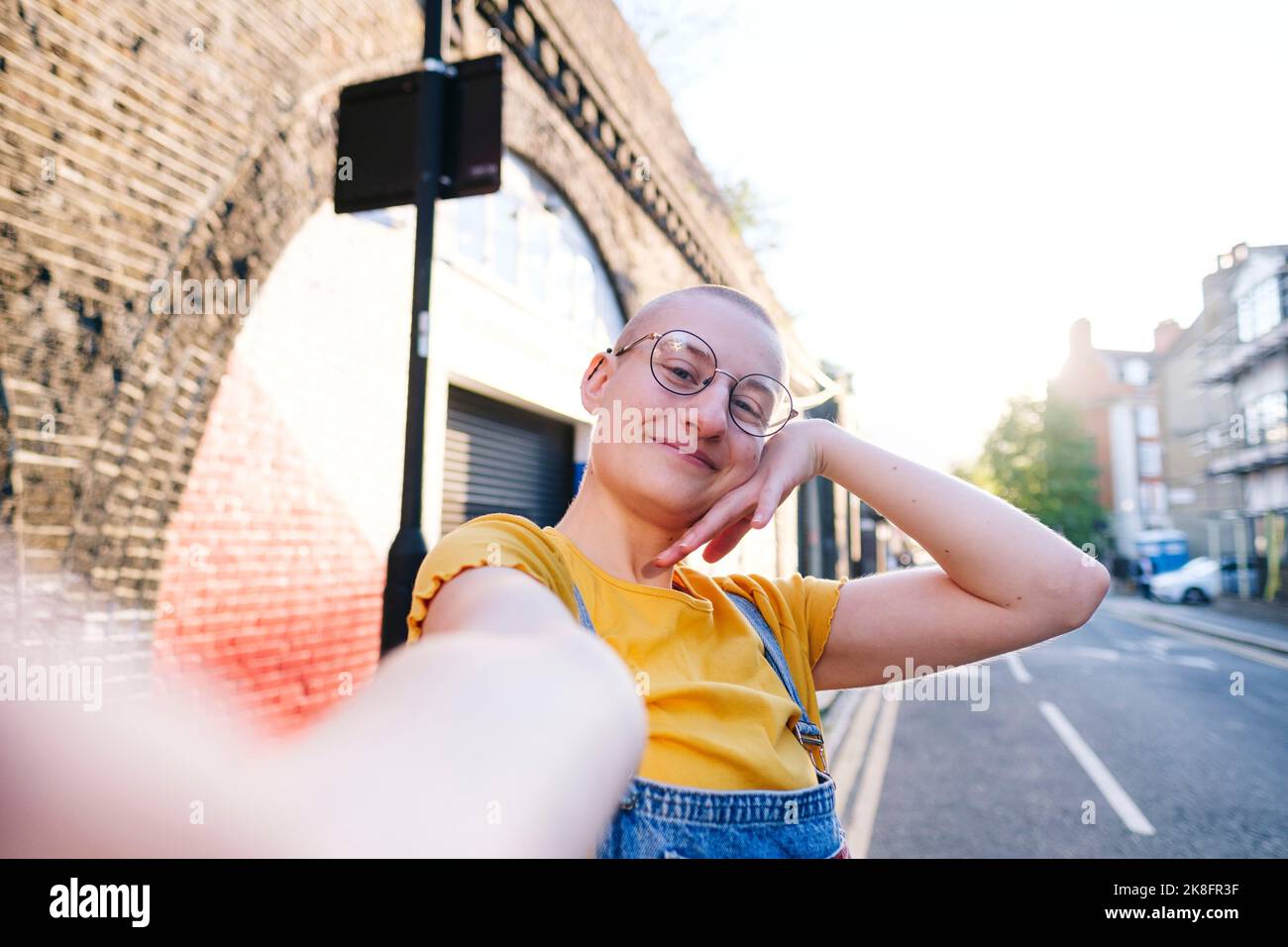 Smiling non-binary person with shaved head taking selfie on street Stock Photo