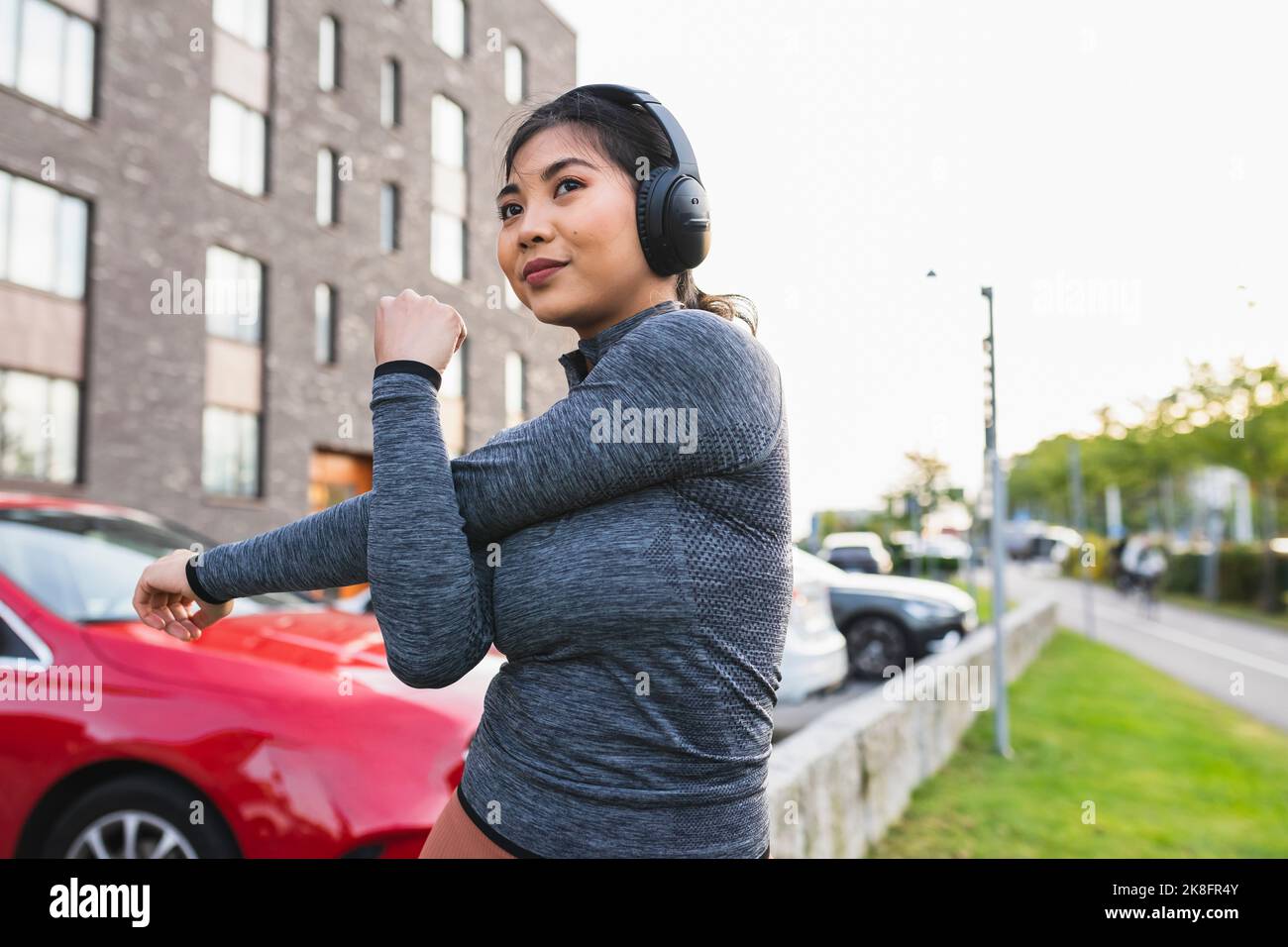 Young woman listening to music and doing stretching exercise on footpath Stock Photo