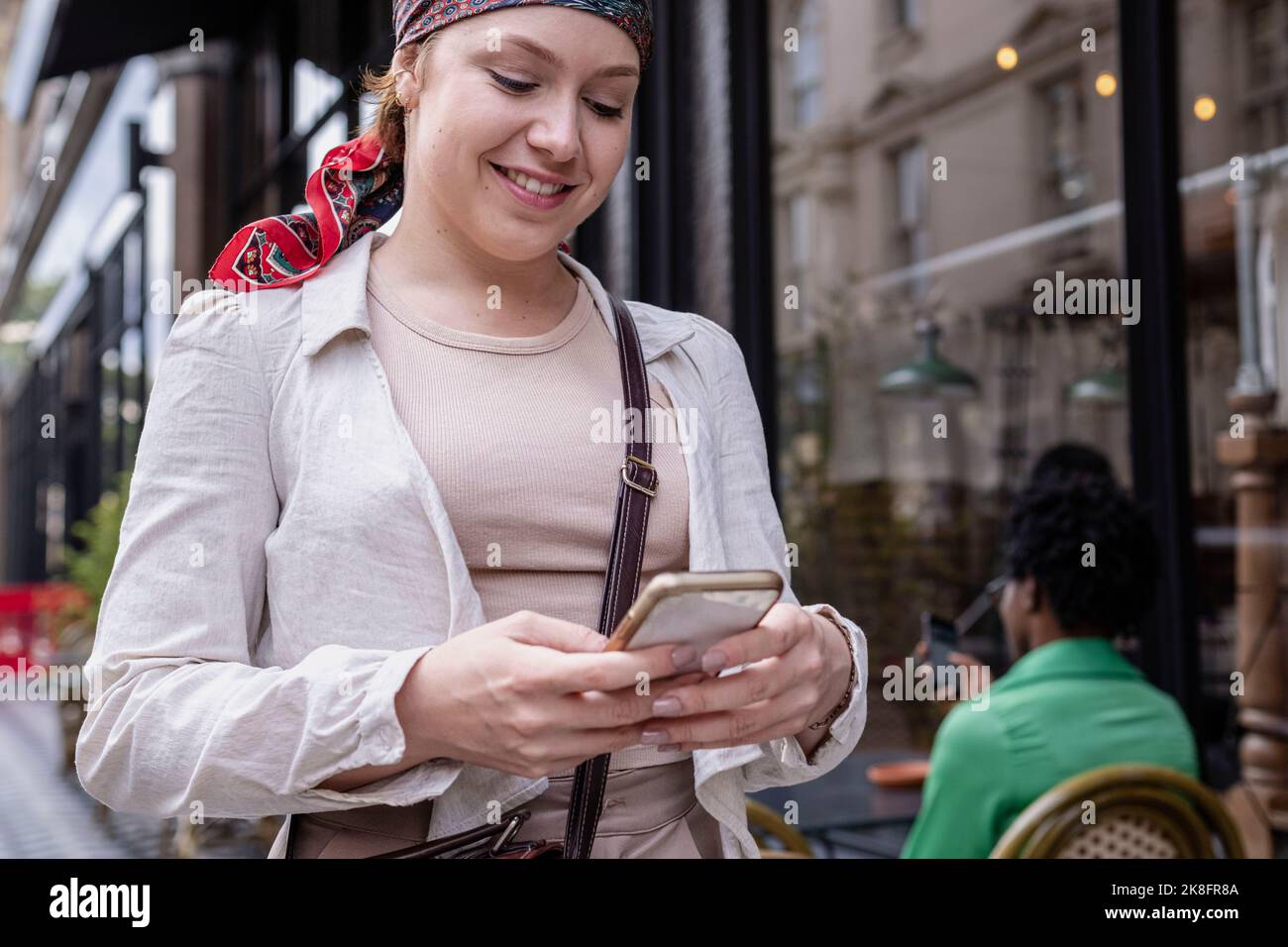 Happy young woman wearing bandana using smart phone at sidewalk cafe Stock Photo