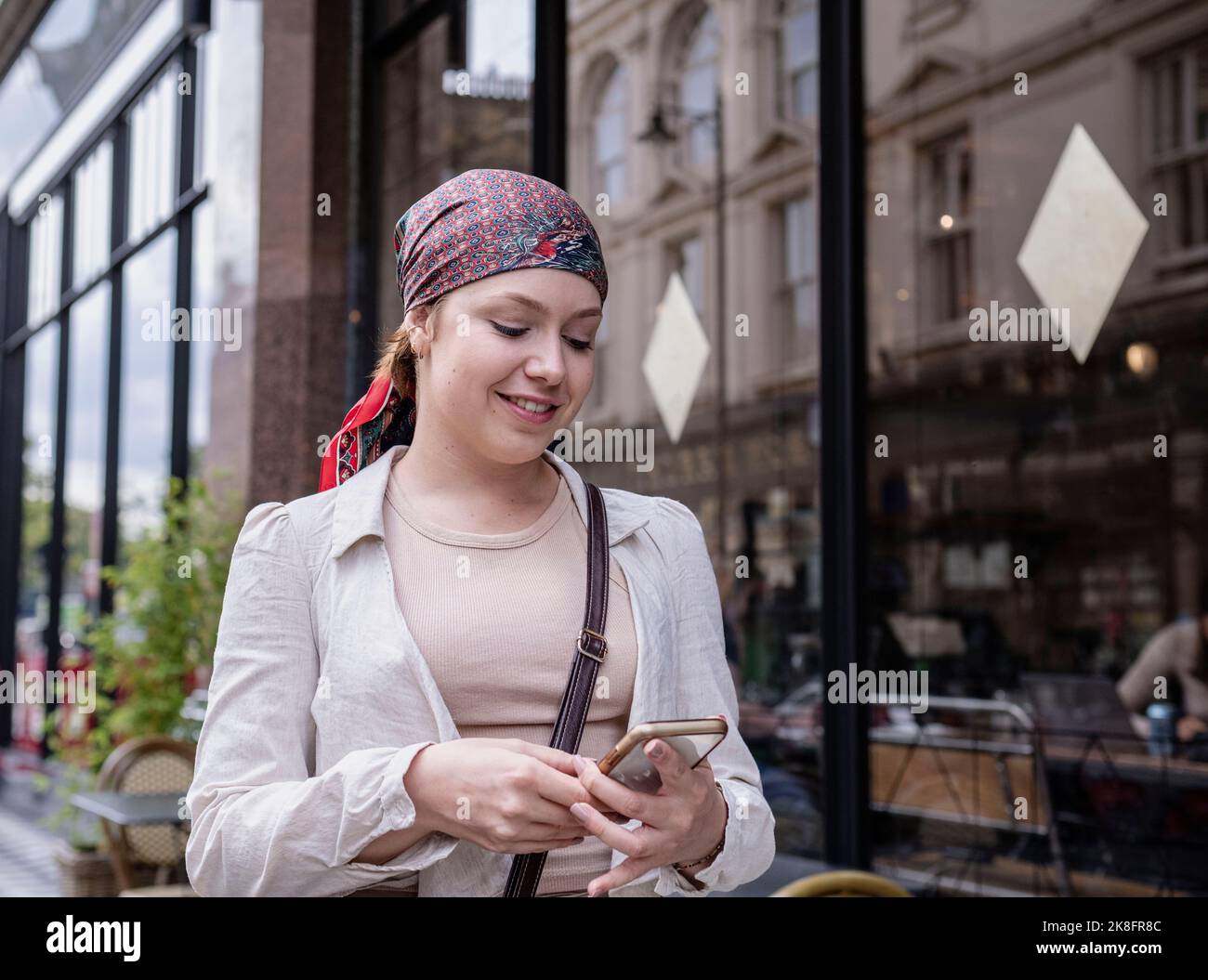 Happy woman wearing bandana using smart phone at sidewalk cafe Stock Photo