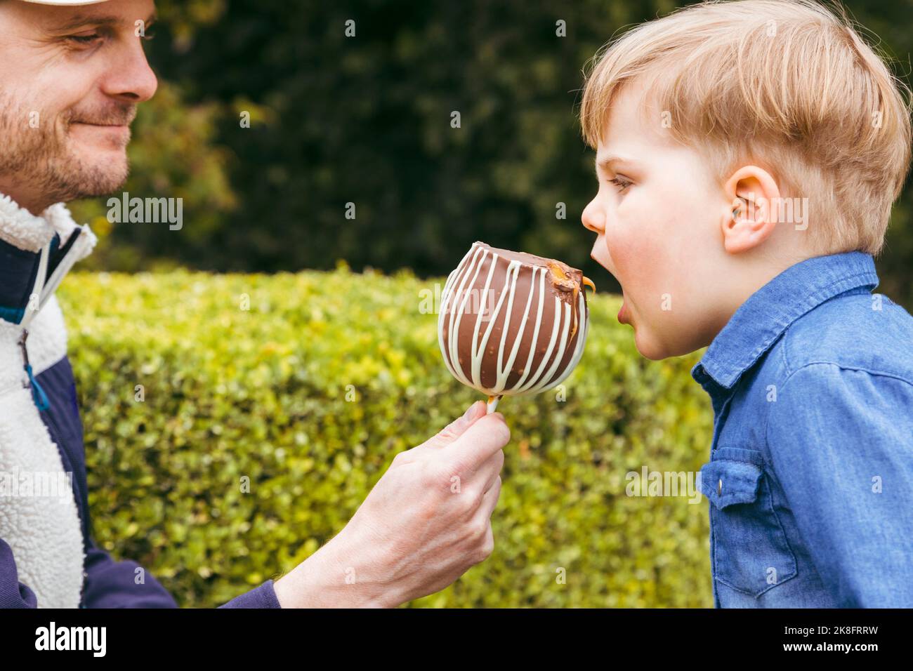 Smiling father feeding taffy apple to son at park Stock Photo