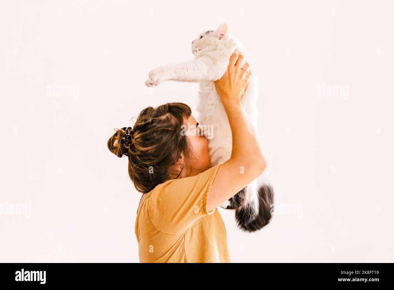 Woman holding aloft cat in front of wall at home Stock Photo