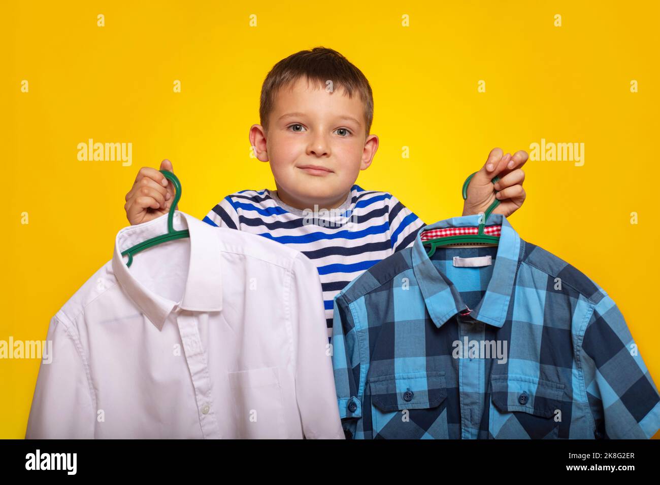 Cute little kid boy trying to decide between two shirt on yellow ...
