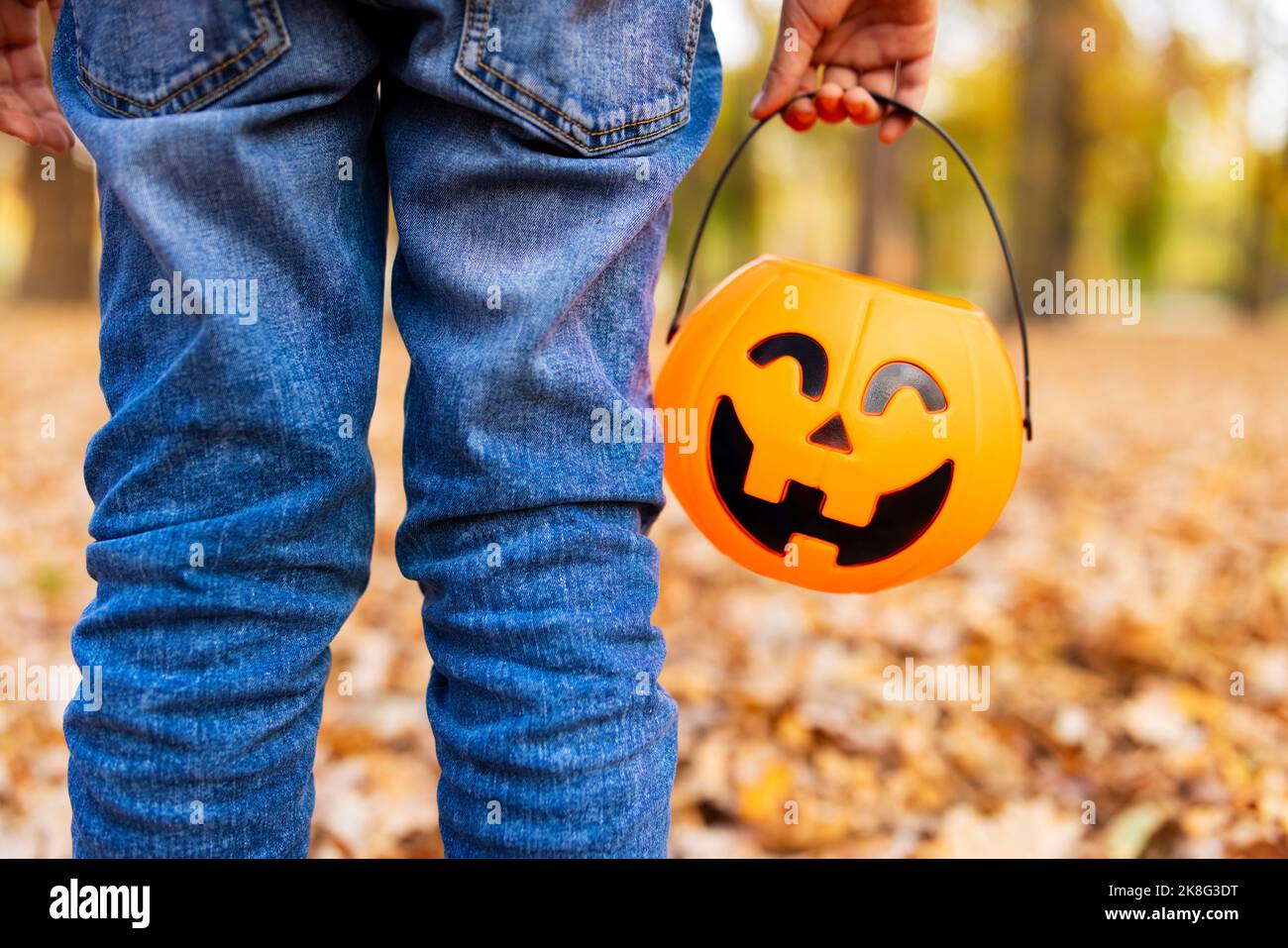 Child holds a bucket shaped like a halloween pumpkin jack o lantern