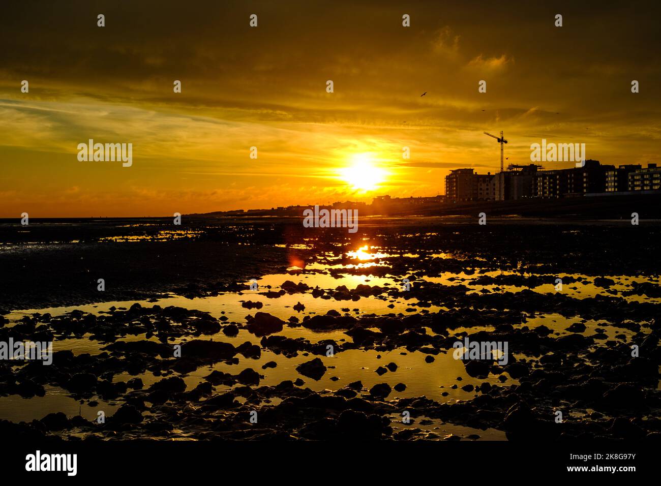 Sun sets over Worthing seafront with building works and cranes on a