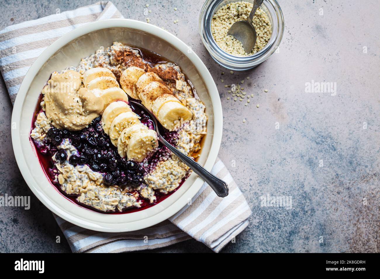 Winter breakfast concept. Overnight oatmeal with banana, berry, chia seeds, sesame tahini, cinnamon and syrup in bowl, top view, dark background. Stock Photo