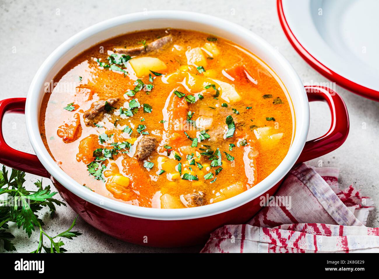 Beef meat slow-cooked soup with carrot, potato, corn and sweet potato in red saucepan. Winter comfort food concept. Stock Photo