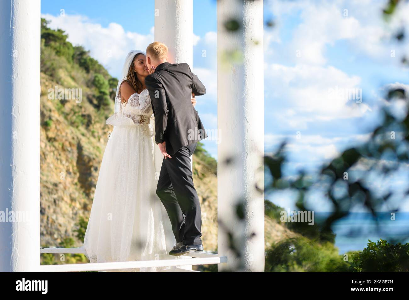 Happy newlyweds kiss in a beautiful gazebo with columns against the ...