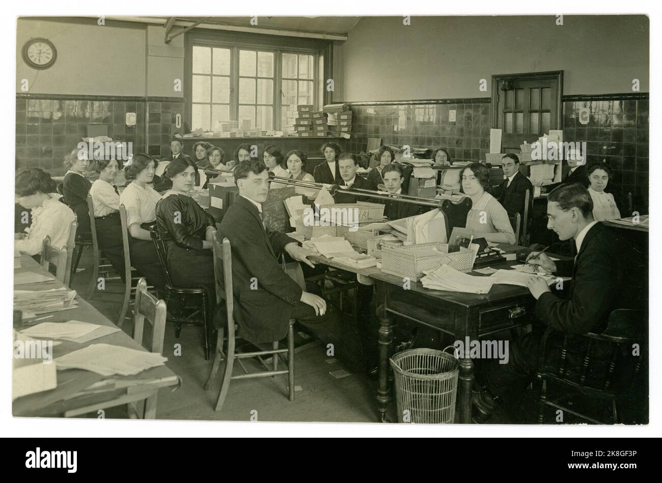 Original early 1900's, WW1 era postcard of young office workers, admin clerks, accounts/ administration staffed with both male and female workers in a large busy and cramped office, lots of paperwork.  U.K. circa 1913 Stock Photo
