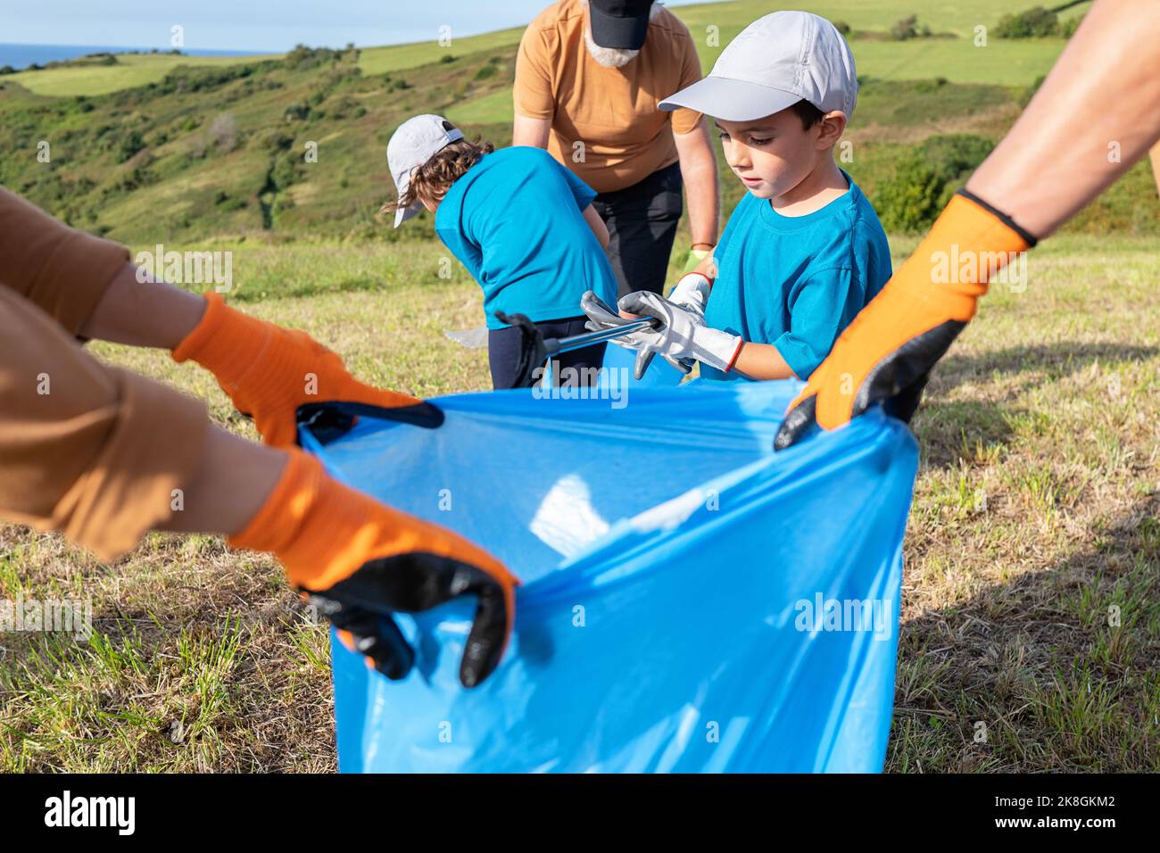 Eco friendly family in caps picking garbage via thrash tongs into blue