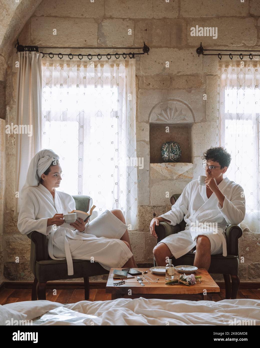 Positive young traveling couple on white bathrobes sitting on