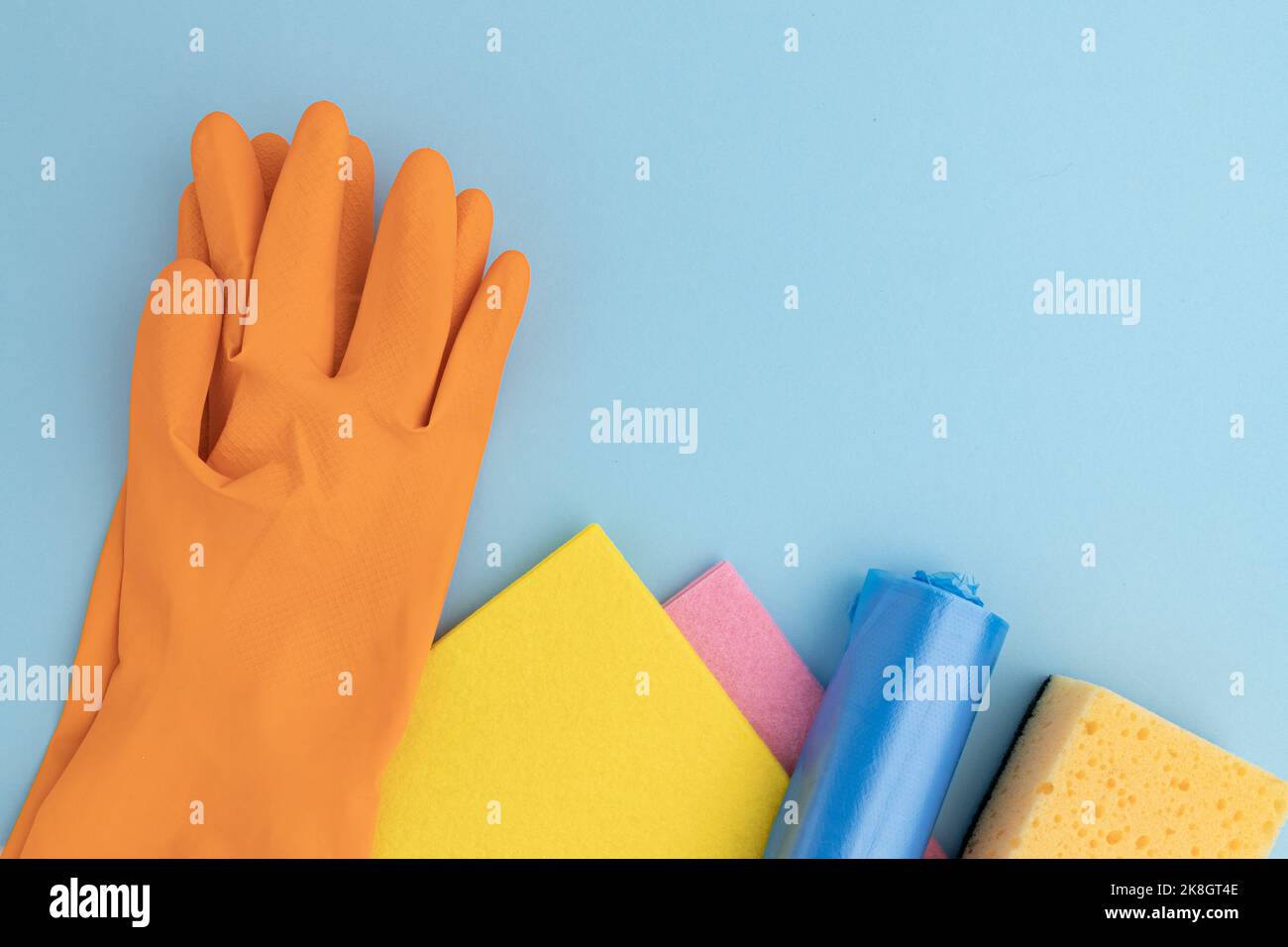 sponge for washing dishes, colored microfiber rags and rubber gloves, garbage bags laid out with frame on blue background, cleaning tools concept with Stock Photo