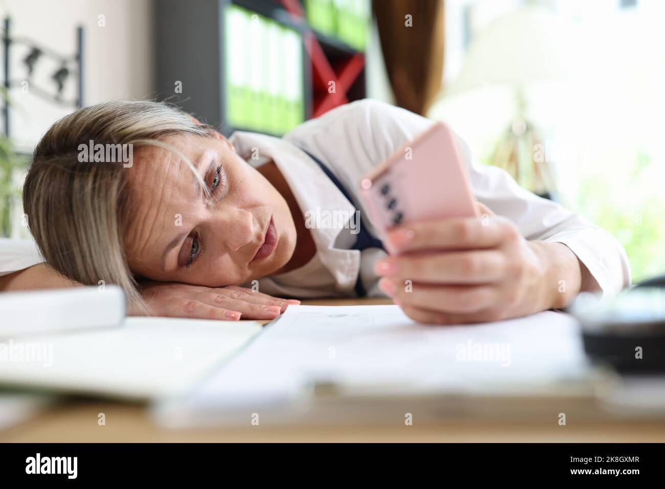 Tired doctor putting head on table and surfing internet on smartphone Stock Photo