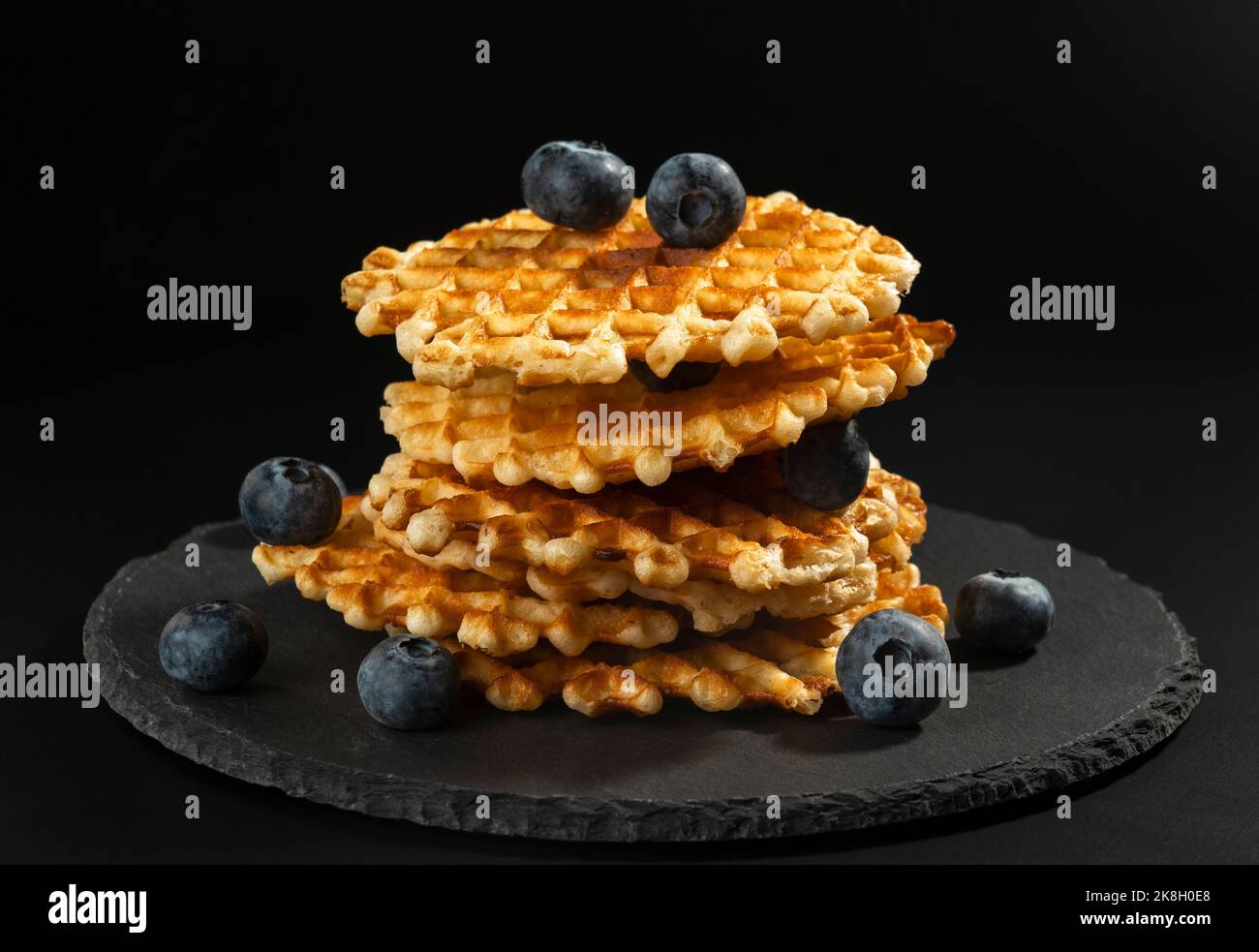 Fresh crispy with a golden crust Belgian waffles with blueberries on a black stone plate on a black background Stock Photo