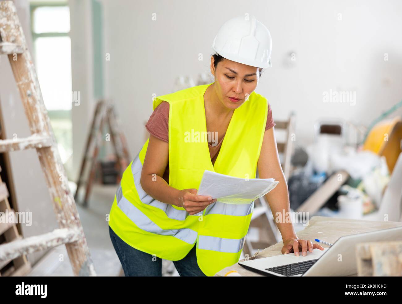Woman builder checking project documentation and using laptop Stock Photo