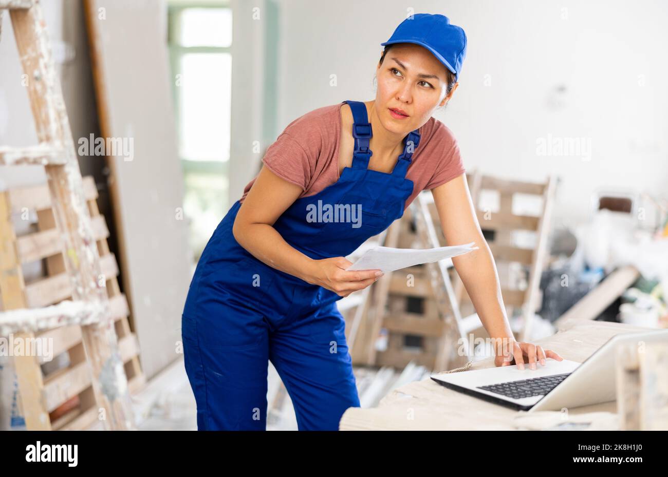 Woman builder checking documentation, using laptop Stock Photo