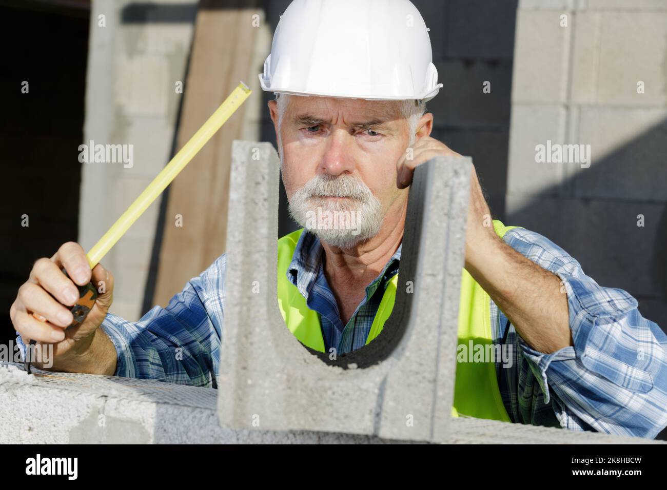 builder in a helmet measuring a cement block Stock Photo Alamy