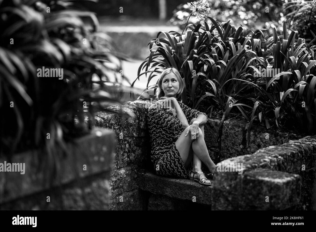 A woman sitting on a stone bench in an old park. Black and white photograph. Stock Photo