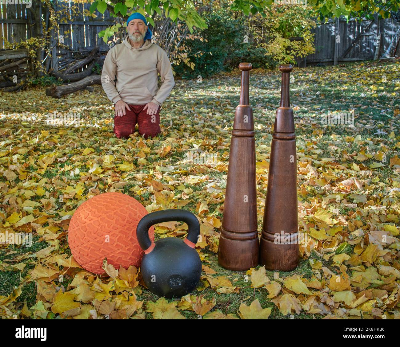 heavy iron kettlebell, slam ball and wooden Persian clubs in a backyard with a senior male seiza sitting in a background, fall scenery Stock Photo