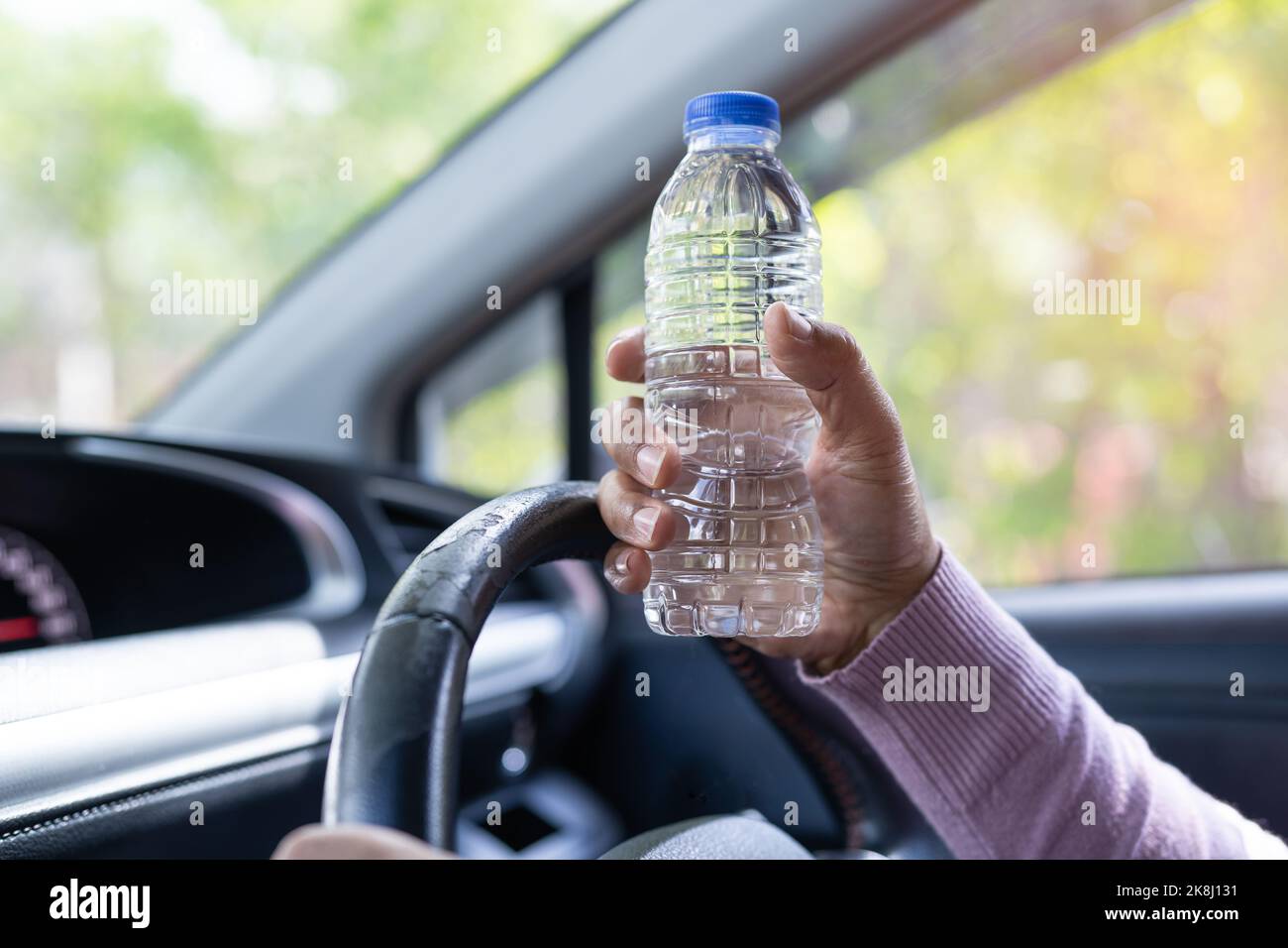 Asian woman driver holding bottle for drink water while driving a car