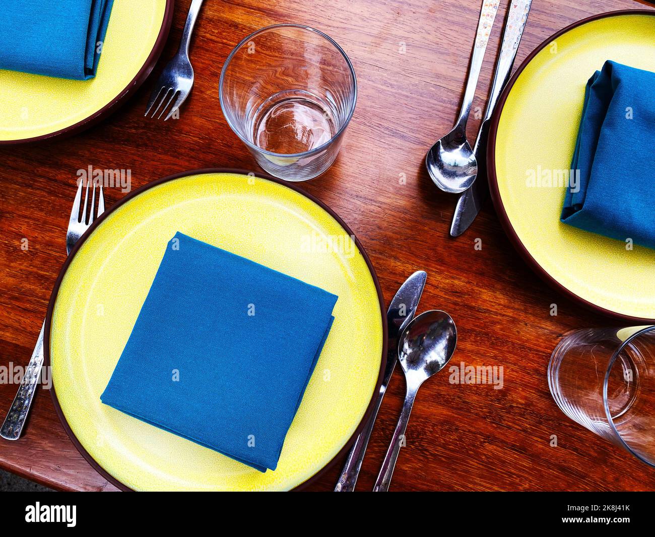A place setting with blue napkins and yellow plates. Colorful Instagrammable hip restaurant table layout Stock Photo