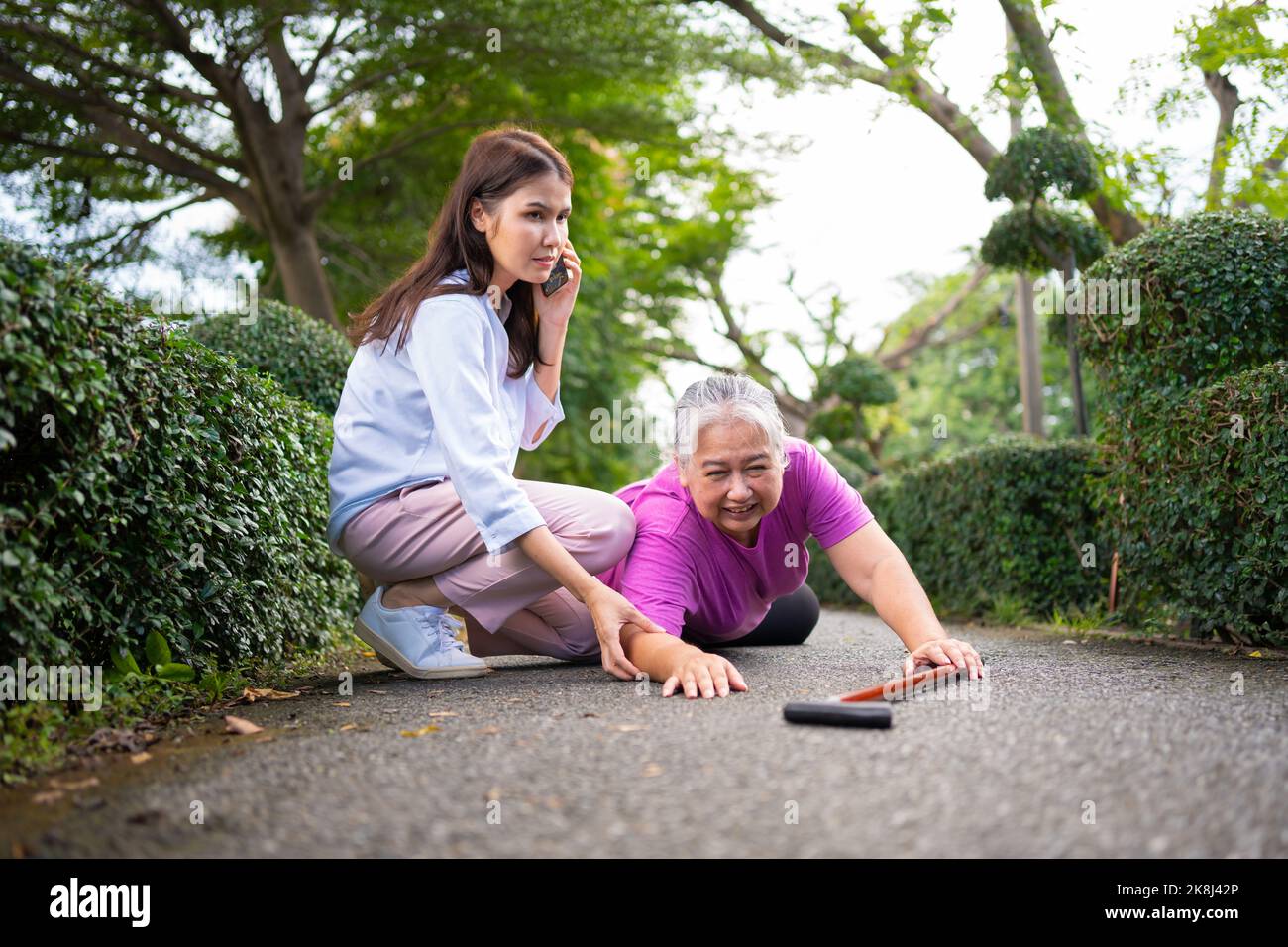 Asian senior woman fell down on lying floor because faint and limb weakness and pain from accident and woman came to help support and call emergency. Stock Photo