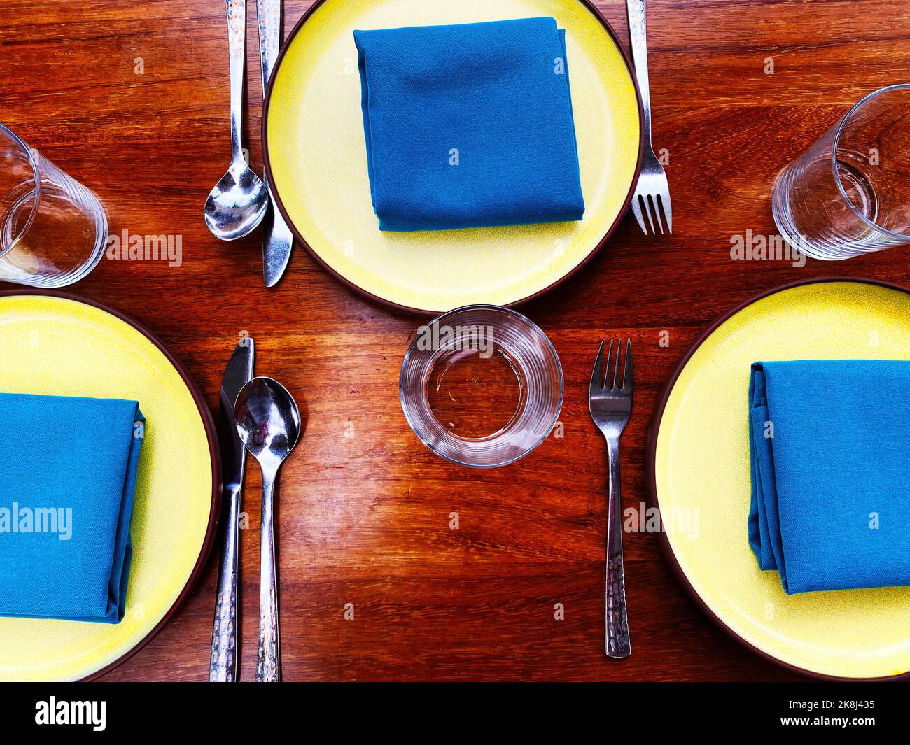 A place setting with blue napkins and yellow plates. Colorful Instagrammable hip restaurant table layout Stock Photo