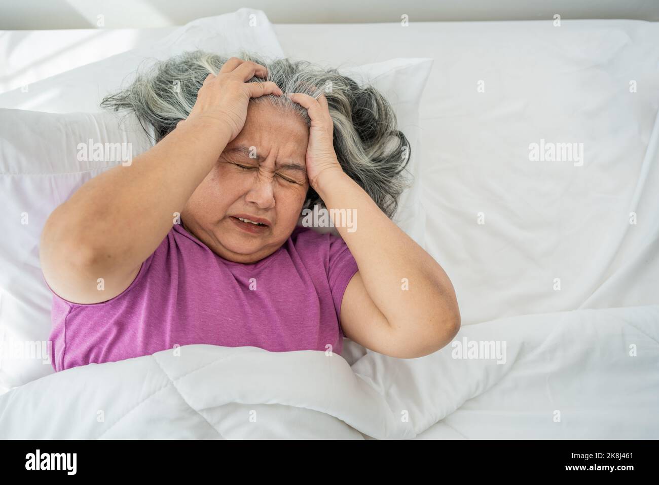Senior woman with gray hair in bed feel depressed or suffering from strong headache migraine and high blood pressure, insomniac trying to sleep distur Stock Photo