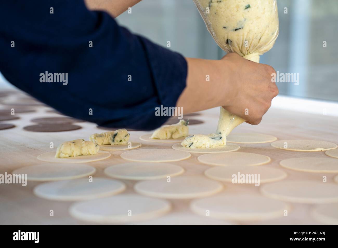 Woman prepare fresh made ravioli inside pasta factory. Using a pastry bag or sac a poche to make stuffed pasta ravioli, culurgiones, agnolotti. Focus Stock Photo