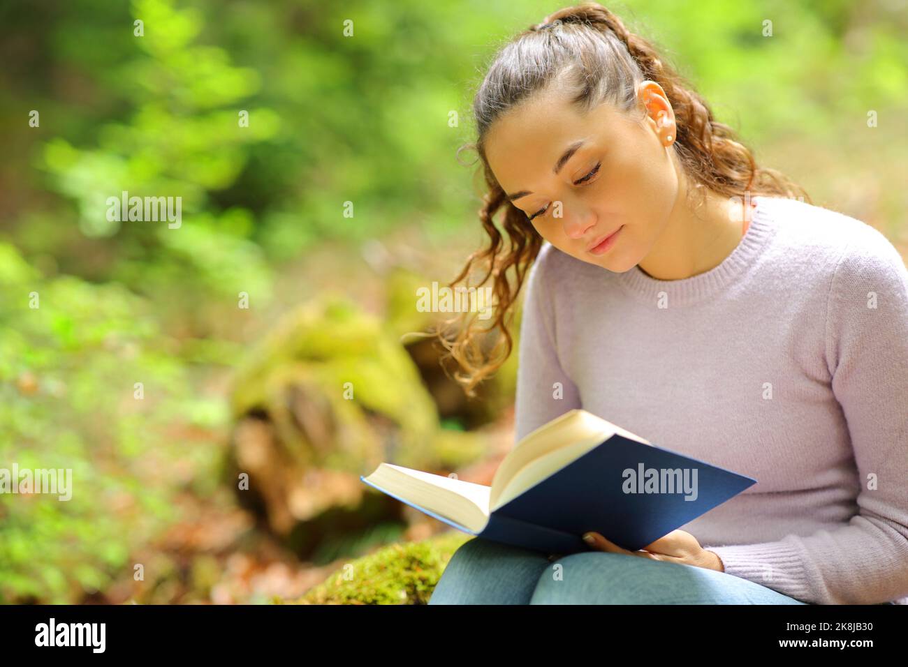 Concentrated woman reading a paper book sitting in nature Stock Photo