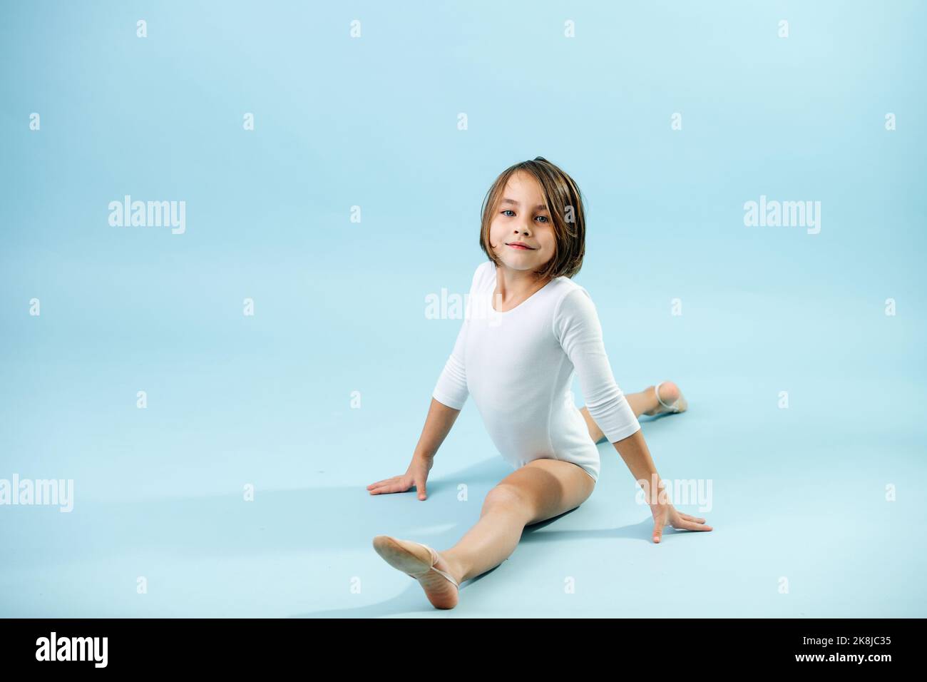 8 yo 8yo girl in a white leotard doing splits, looking at the camera. Over blue  background Stock Photo - Alamy
