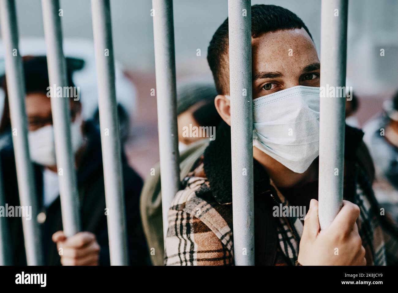 We need a saviour. a young man wearing a mask while stuck behind a gate in a foreign city. Stock Photo
