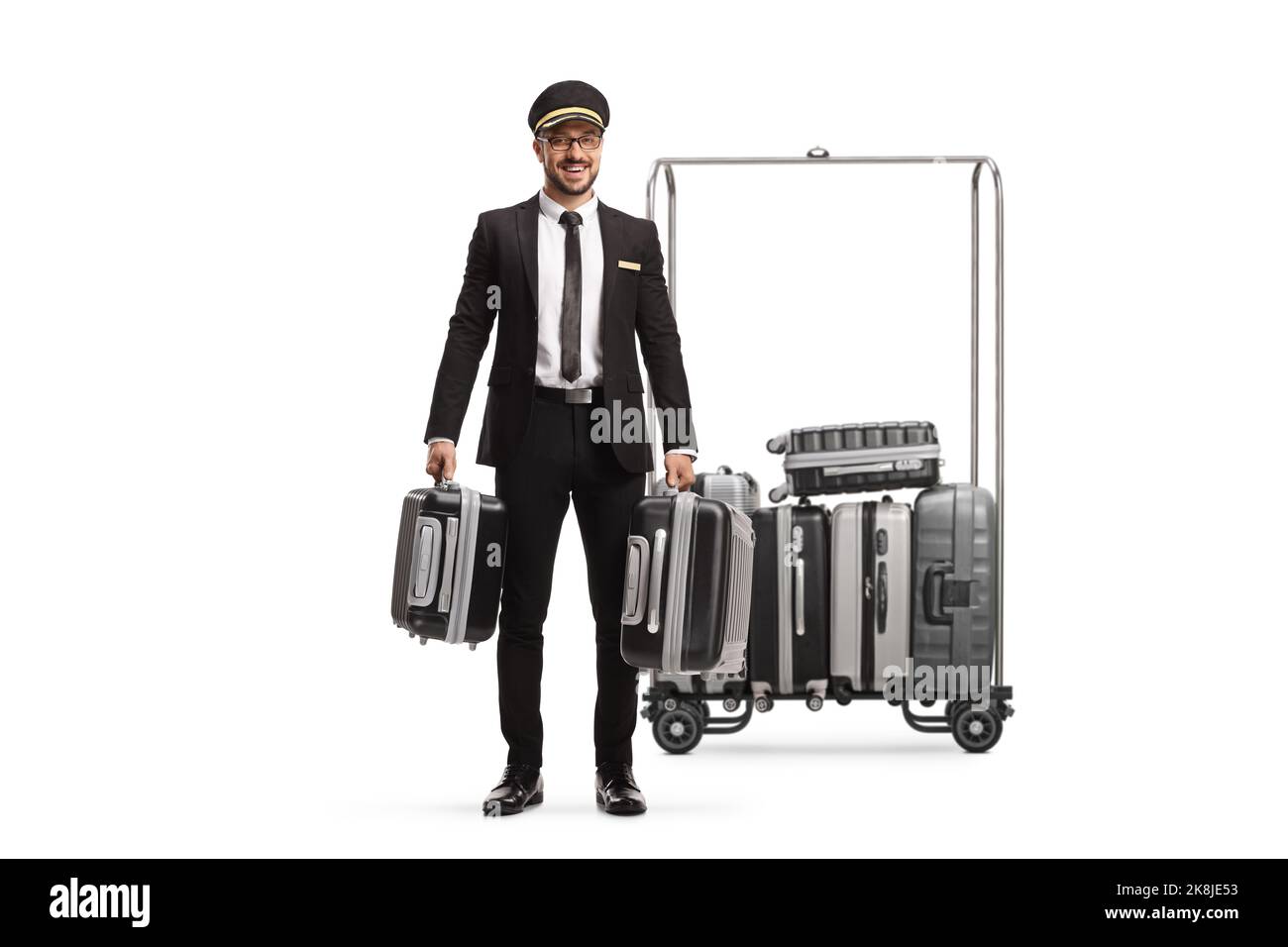 Bellboy holding suitcases and standing next to a luggage cart isolated