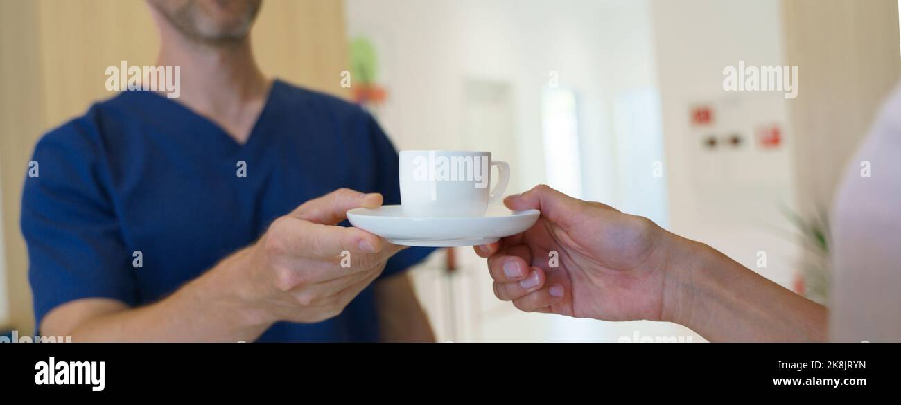 Close-up of dentist giving cup of coffee to patient, private dental clinic. Stock Photo
