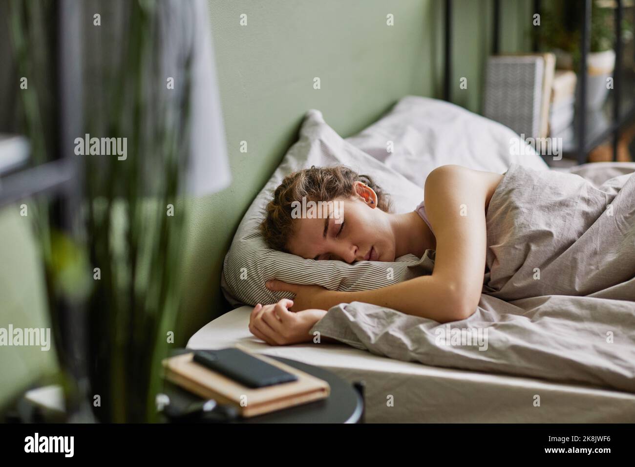 Young woman sleeping on pillow under blanket in her bed in bedroom