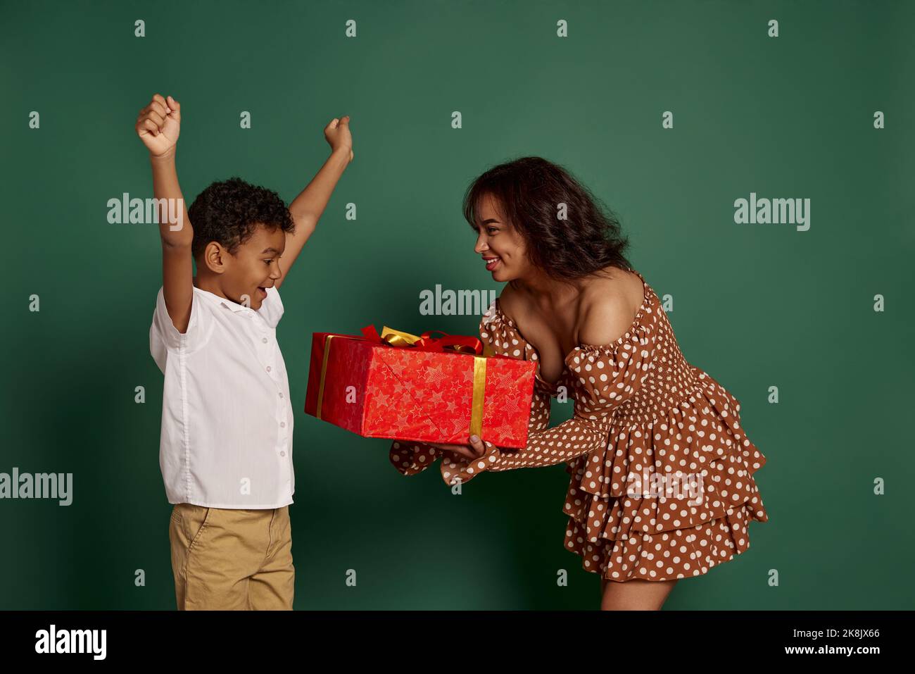 Portrait of young woman giving box present box to teen boy over green ...
