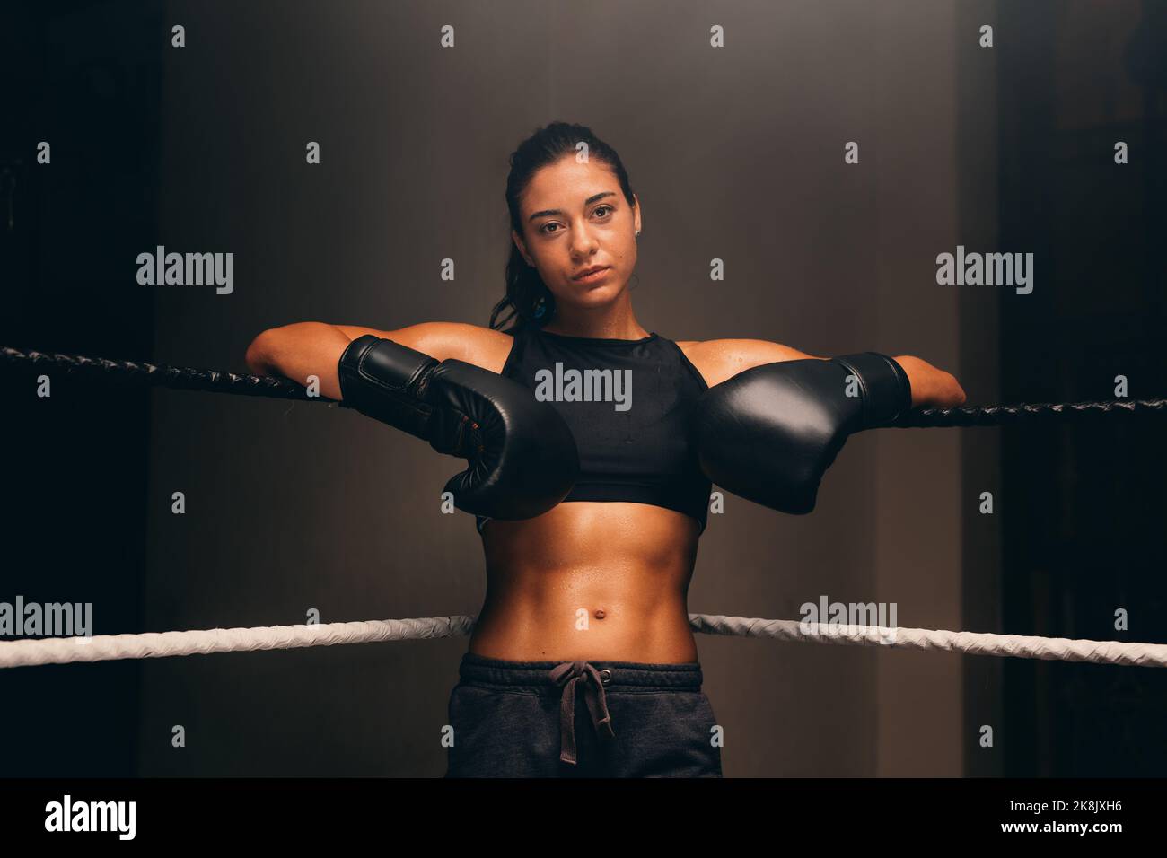 Confident boxer looking at the camera while leaning against the ropes of a boxing ring in a gym