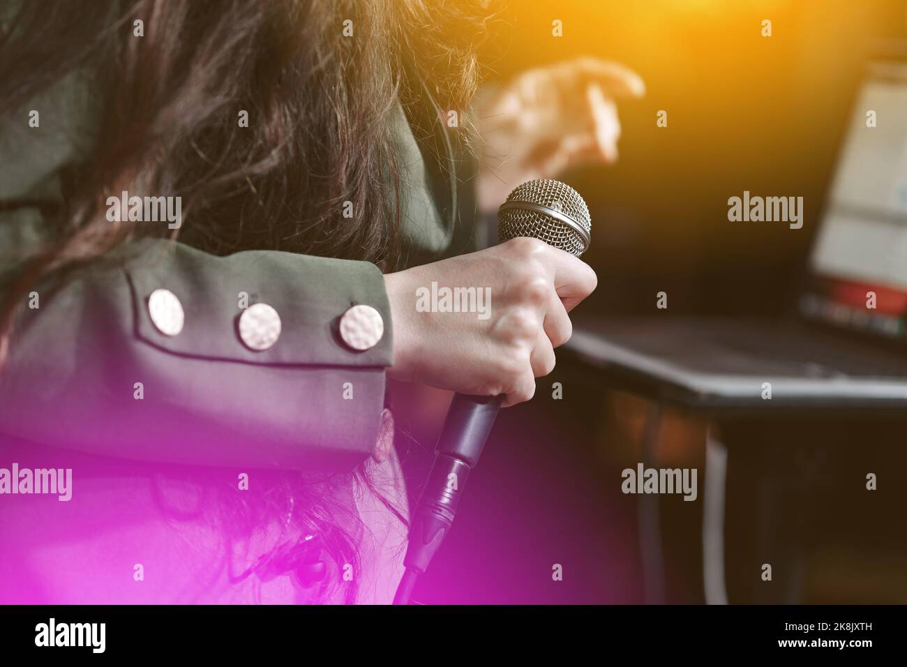 close up female hand holding microphone on music hall. cropped image of female singer in green jacket, holding mic Stock Photo
