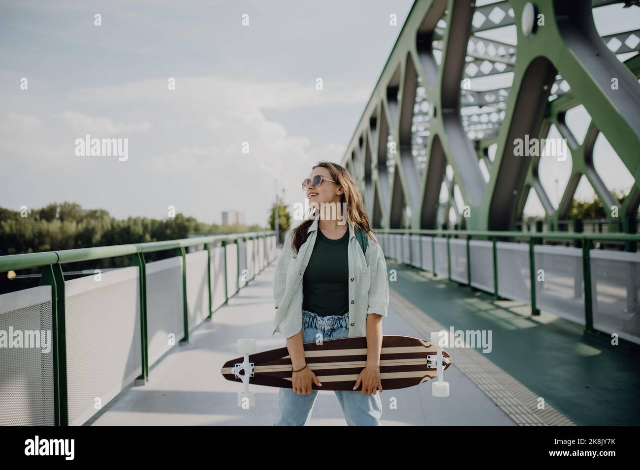 Young woman walking on city bridge with skateboard. Youth culture and commuting concept. Stock Photo