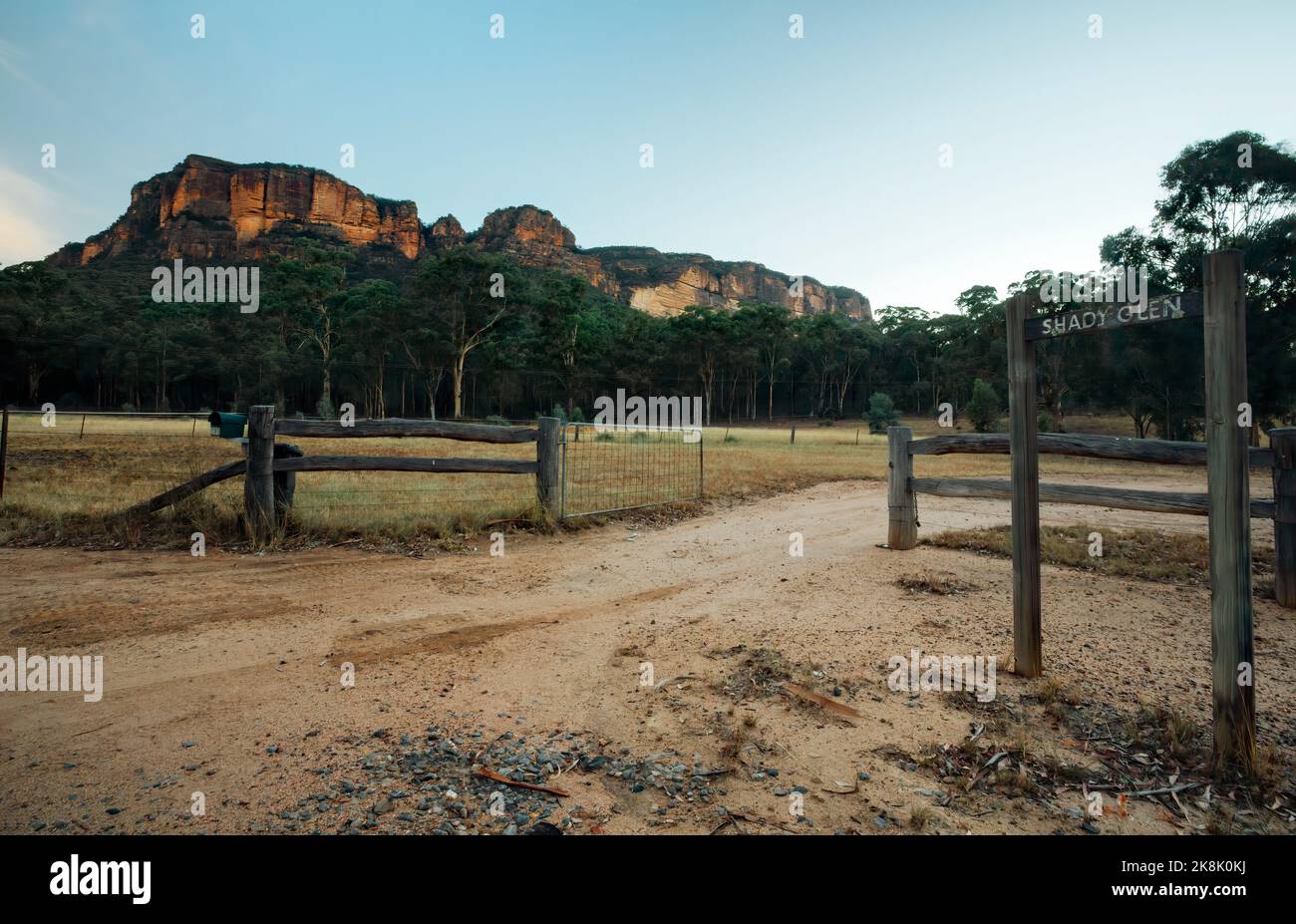Sheer rsteep ocky mountains rise up from the Capertee Valley on all sides.  An open gate entrance to a farm where cattle grase  the surrounding area i Stock Photo