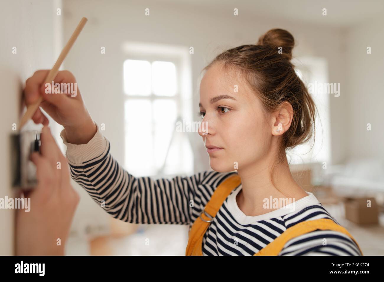 Young woman remaking her apartment, measuring wall with spirit level and hanging shelf. Stock Photo